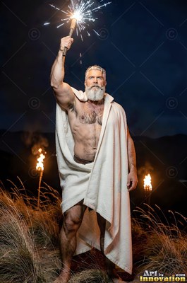 Holding a sparking torch high, a full-bearded man stands on a hill in a white robe
