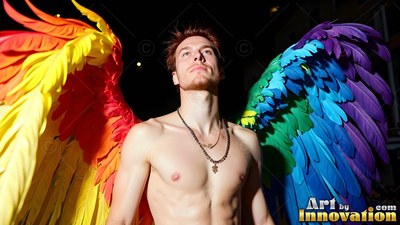 Looking upward at night, a shirtless man stands in broad rainbow feather wings