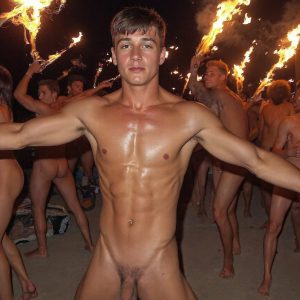 Bad Boys Naked Beach Party II. A full-body composition of a nude young man standing near a crackling bonfire, on a serene moonlit night at the beach. The gentle glow of the flames, flickers across his shinny wet body, catching his contours, and highlighting his muscular physique and handsome face. People everywhere partying, dancing to the music, having a good time together, naked, and free.